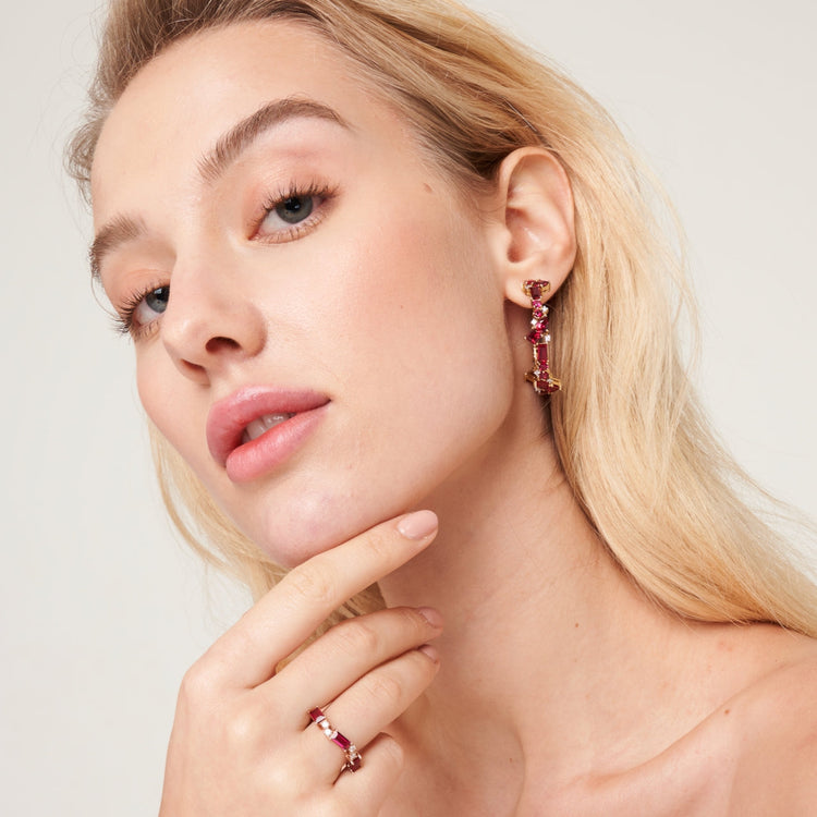 A model wearing Lanna large hoop earrings set with lab grown diamond and ruby gem stones. She also wear baguette Forma ring set with lab grown ruby and diamonds.